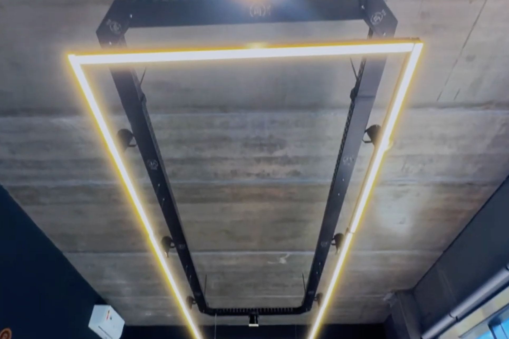Eletrocalha preta suspensa no teto de concreto aparente, com uma moldura de luz em volta.